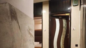 Pasillo de hotel con paredes de mármol, una puerta de madera con un panel decorativo y una escalera que lleva a una habitación con cama.