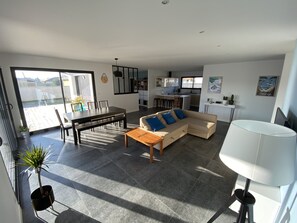 Un salon moderne avec un canapé, une table à manger et des chaises. Il y a également un coin cuisine avec un bar et une table à manger. La pièce est dotée de grandes fenêtres et offre une vue sur l'extérieur.