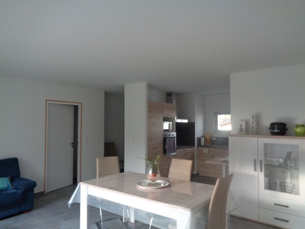 Een moderne keuken met witte kastjes, een magnetron en een fornuis. Er is een eethoek met een tafel en stoelen, en een blauwe bank in de hoek.