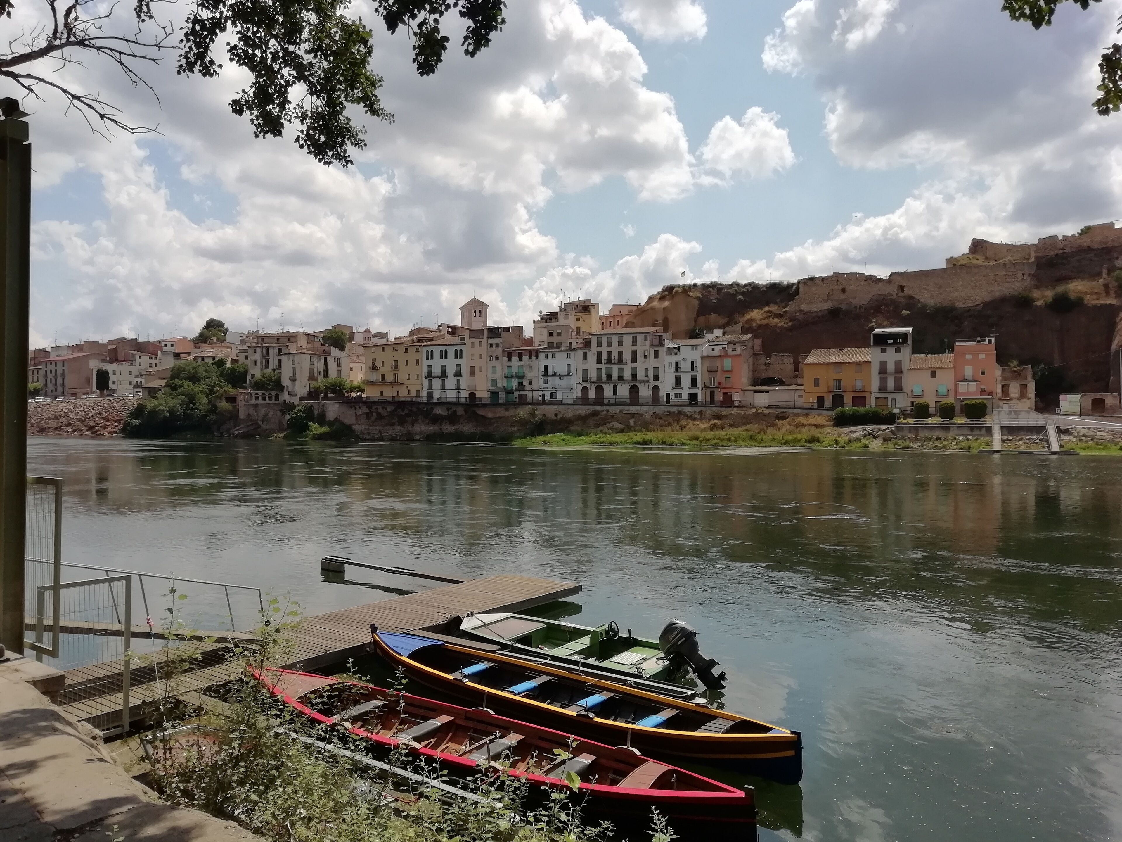 A riverside view with boats docked, a bridge, and buildings along the riverbank.