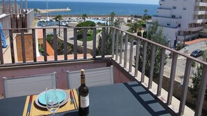 Un balcón con una mesa preparada para dos personas, con vistas a un puerto deportivo y al mar.