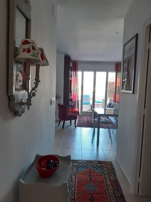 A hallway with a dining area, a red chair, a table, and a patterned rug.