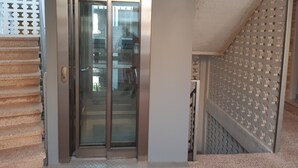 Un ascensor moderno con puertas de vidrio, un agarrador metálico y una pared texturizada a su lado.