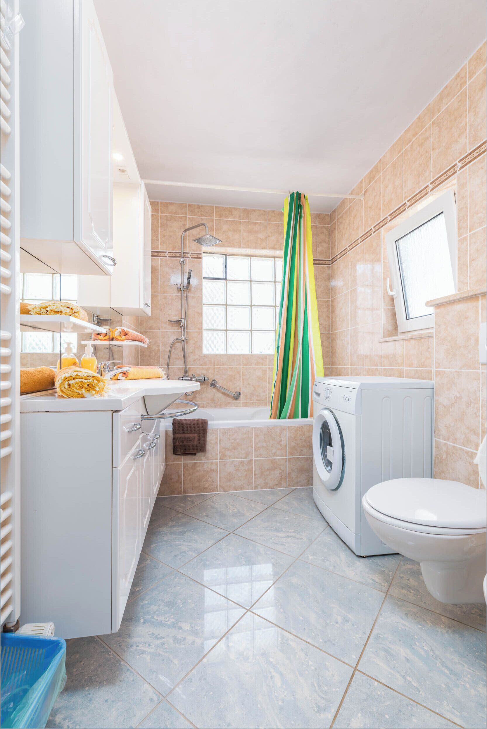 Een badkamer met een wasmachine, toilet en een douche met een streepjesgordijn.