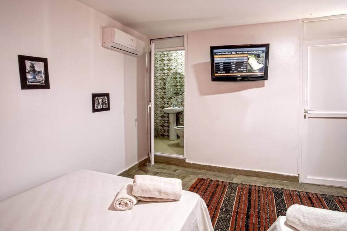Habitación de hotel con cama, televisor montado en la pared, puerta que da a un baño y una ventana pequeña.