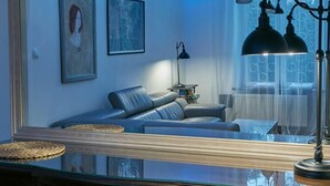 A living room with a sofa, two framed artworks, a lamp, and a window with curtains.
