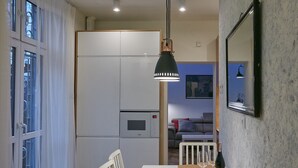 A compact kitchen with a refrigerator, dining table with cork placemats, and a hanging pendant light.