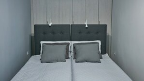 A double bed with a grey headboard and two pillows, set against a grey wall with a vertical panel design.
