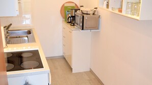A compact kitchen with a stove, sink, and microwave. There is a shelf with glasses and a coffee maker.