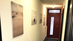 A hallway with a wooden floor, a red door at the end, and three framed pictures on the wall.