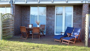A patio with a brick wall, a wooden table with chairs, and two blue lounge chairs.