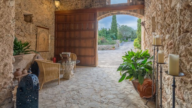 Un'accogliente stanza in pietra con una porta in legno che dà sull'esterno, mobili in vimini e una pianta in vaso.
