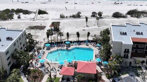 Un complexe hôtelier doté d’une piscine entourée de chaises longues et de parasols, avec une plage en arrière-plan et des palmiers.