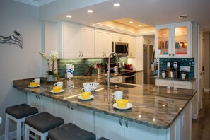 Una cocina moderna con armarios blancos, una isla central con taburetes altos, un microondas y un refrigerador.