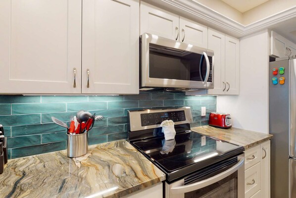 A kitchen with white cabinets, a stainless steel microwave, a black stove, and a red toaster. - Stunning Decor, Outstanding Views, Private, On the Beach, Pool, Tennis, Hot Tub, Parking, & Gated. (Treasure Island)
