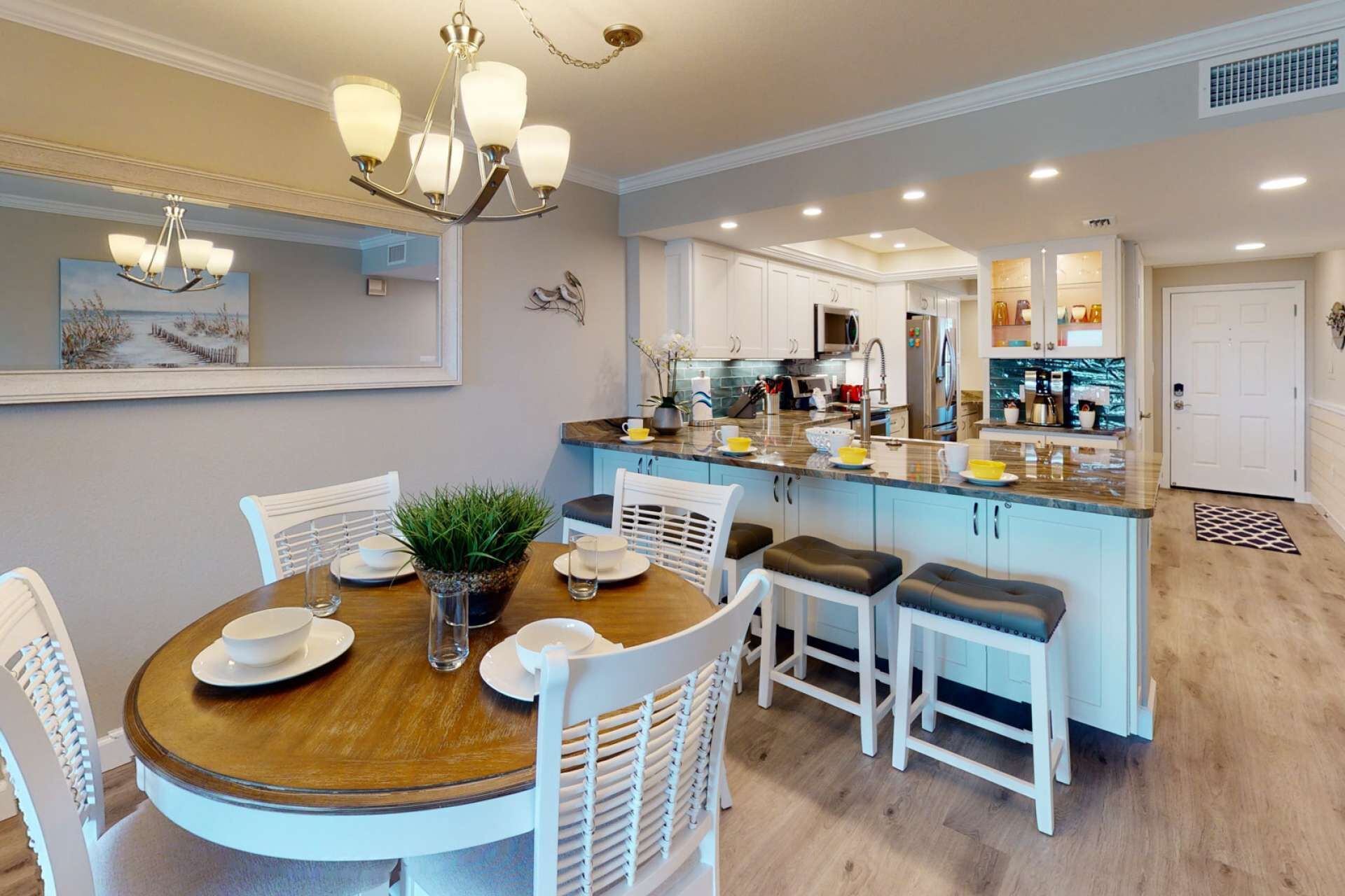 A modern kitchen with white cabinets, a central island, and a dining area with a round table and white chairs.