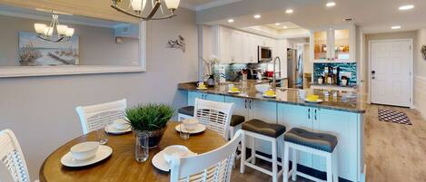 A modern kitchen with white cabinets, a central island, and a dining area with a round table and white chairs.
