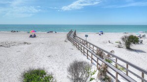Une plage avec une promenade en bois menant à l’eau, des parasols et des chaises de plage.