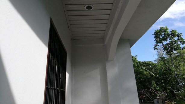 A building's exterior with a white facade, a window with metal bars, and a ceiling with a vent. - Siargao Hannah House (Surigao city)