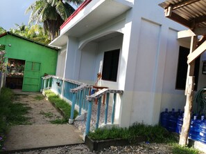 Un edificio con fachada blanca, barandilla azul y un camino empedrado que conduce a una puerta verde.