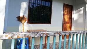 A room with a tiled floor, a window with bars, a wooden door, and a blue stool. - Siargao Hannah House (Surigao city)