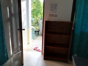 Una habitación con un estante de madera, una puerta que da al exterior y un cartel en la pared.