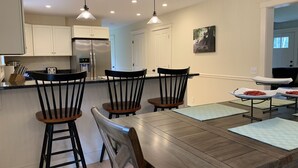 A modern kitchen with a wooden dining table, black chairs, and a refrigerator. - Newly built and fresh vacation home tucked in the woods of Mount Desert.  (Mount Desert)