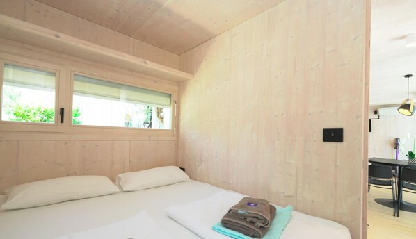 A bedroom with a large bed, two windows, and a view of greenery outside.