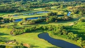 A golf course with multiple ponds and lush greenery, surrounded by mountains.