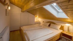 Et hyggeligt soveværelse med ovenlys, en seng med hvide sengetæpper, et natbord med lampe og en radiator.