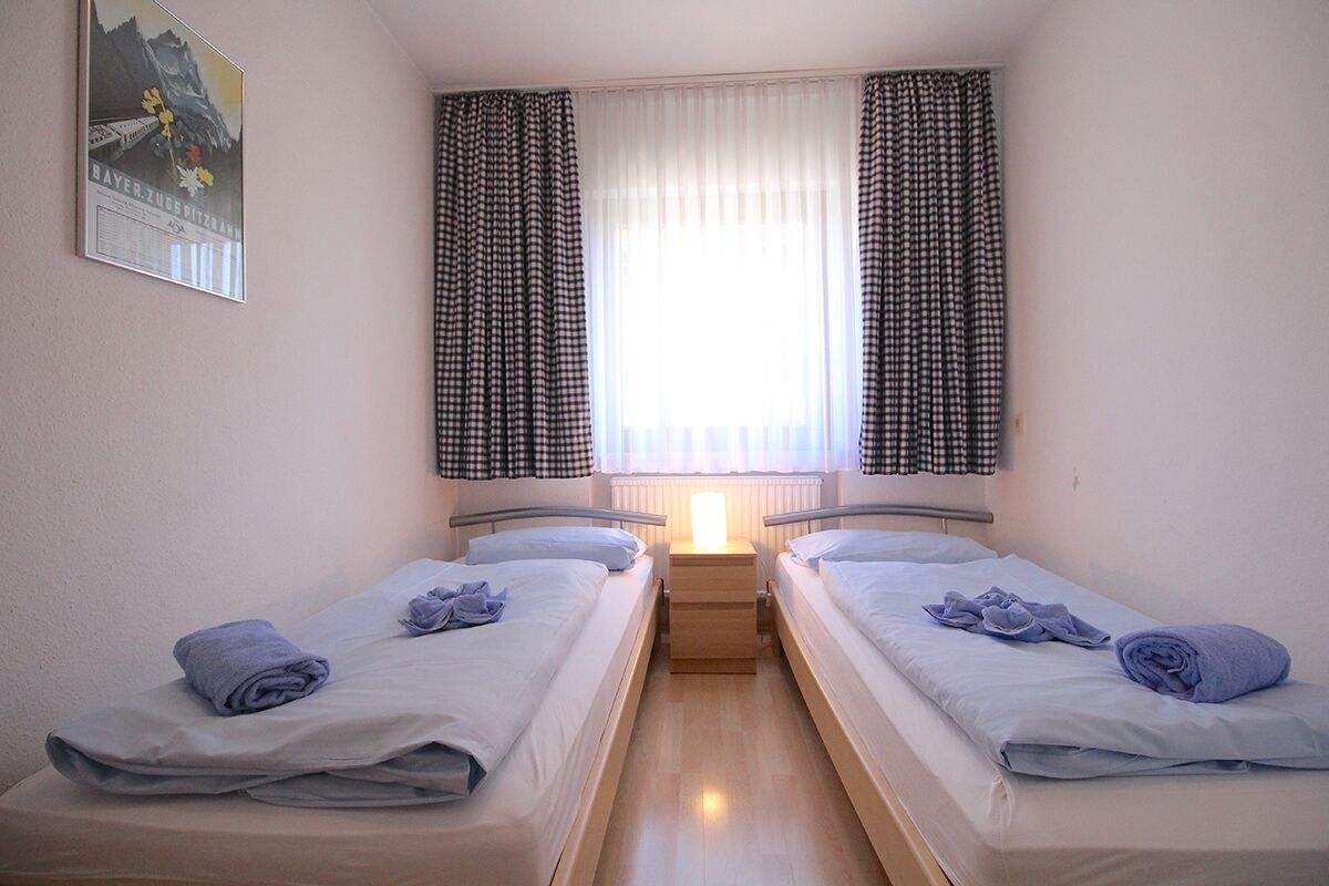 Habitación doble con dos camas individuales, una mesita de noche de madera, una ventana con cortinas a cuadros y un cartel en la pared.