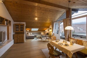 A cozy cabin interior with a dining area, wooden ceiling, and large windows. - Lindenschlösschen & Schlossgarten (Garmisch-Partenkirchen)
