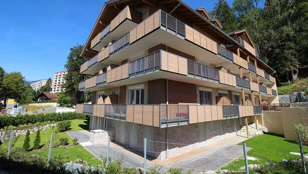 Un edificio de varios pisos con balcones, un jardín ajardinado y cielo despejado.