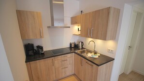 Una cocina compacta con armarios de madera, encimera negra y pileta de acero inoxidable.