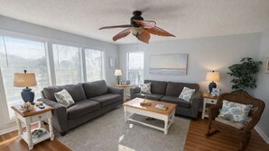 A living room with two grey sofas, a wooden coffee table, a wicker armchair, and a ceiling fan. - Sea Oats I-202. Pool View, Waterfront Access. 1K, 2Q, 1Q sofa bed. (Gulf Shores)