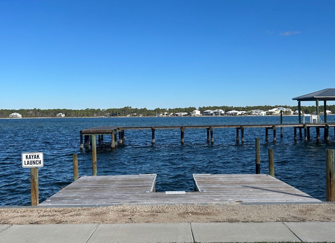 A wooden pier extending into a body of water with a sign indicating a kayak launch point.