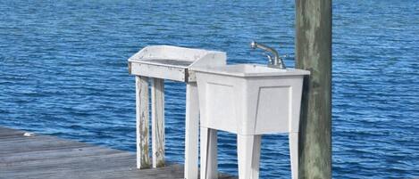 Un muelle de madera con dos lavamanos blancos y un grifo metálico.