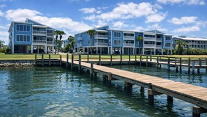 A waterfront hotel with multiple buildings, a wooden dock, and a clear blue sky. - Sea Oats I-202. Pool View, Waterfront Access. 1K, 2Q, 1Q sofa bed. (Gulf Shores)