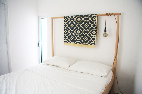 A bed with a wooden frame and white bedding, a patterned throw blanket, and a hanging light fixture.