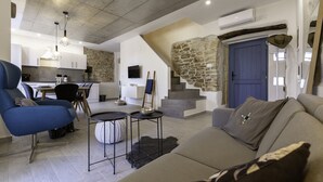 A modern living room with a sofa, a blue armchair, a small table, and a staircase with a stone wall.
