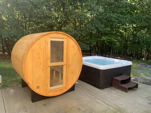 Un tonneau de sauna en bois et un jacuzzi sur une terrasse en bois, avec une forêt en arrière-plan.