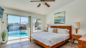 Ein Schlafzimmer mit einem großen Bett, einem hölzernen Kopfteil, zwei Nachttischen inklusive Lampen, einem Gemälde an der Wand und einer Glastür, die zu einem Pool führt.