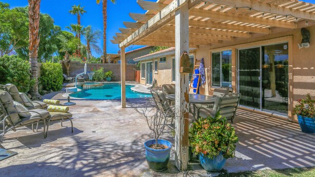 Eine überdachte Terrasse mit Gartenmöbeln, einem Pool und einer Pergola.