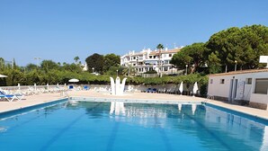A clear blue swimming pool with a central fountain, surrounded by lounge chairs and umbrellas, with a building in the background. - modern, newly renovated apartment in Cabo Roig, beach within walking distance (Orihuela)