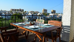 A wooden table set with plates, glasses, and a bowl on a balcony overlooking a coastal town with buildings in the background. - modern, newly renovated apartment in Cabo Roig, beach within walking distance (Orihuela)