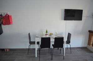 A dining area with a white table set for four, black chairs, a flat-screen TV mounted on the wall, and a red bag hanging on the wall. - modern, newly renovated apartment in Cabo Roig, beach within walking distance (Orihuela)
