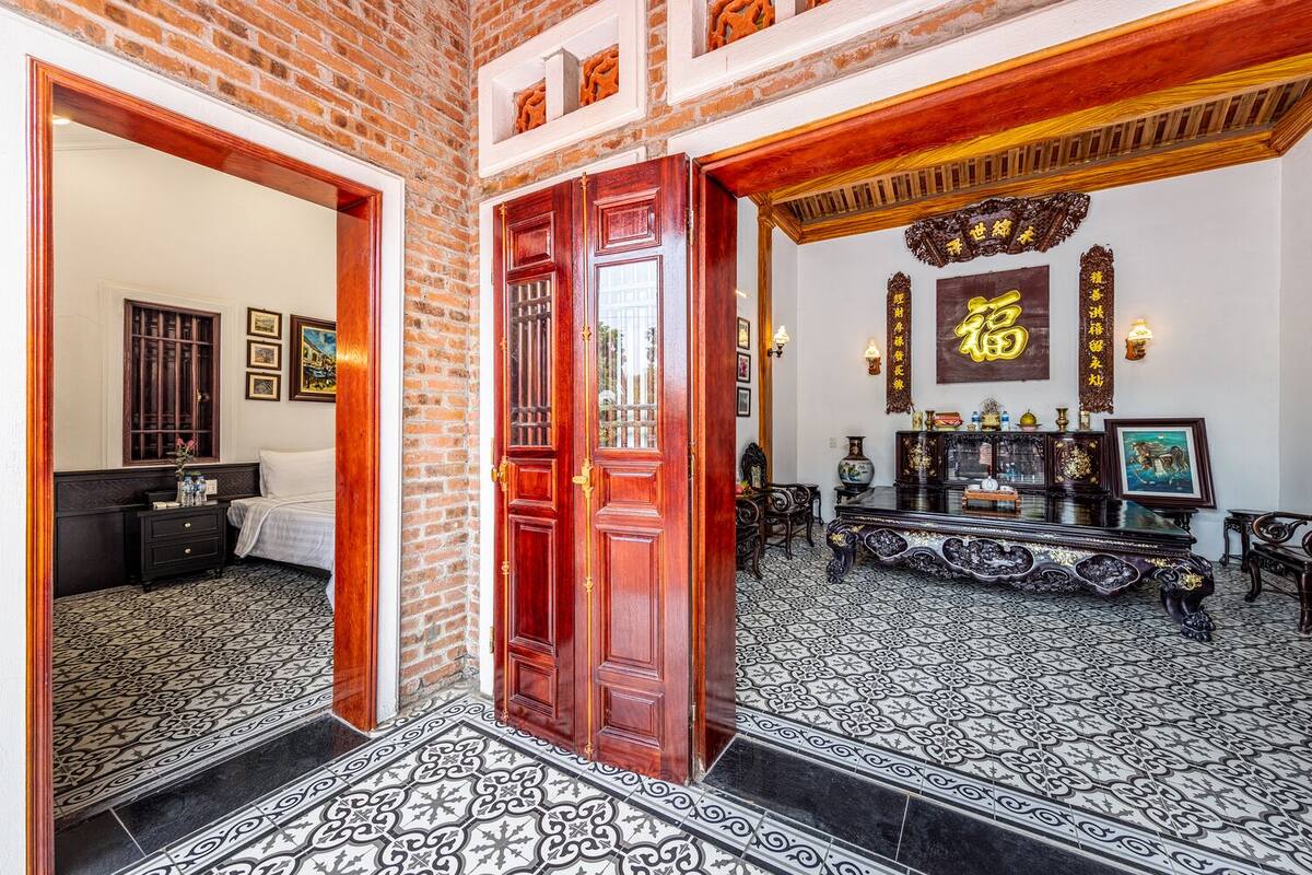 A traditional room with a large wooden door, a bed, a desk with a computer, and a wall with calligraphy.
