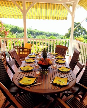 Een ronde houten tafel voor zes personen, met gele servetten, een fruitschaal en glazen.