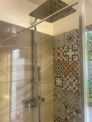 Een douche met een glazen deur, een regendouche en een wand met tegelwerk.