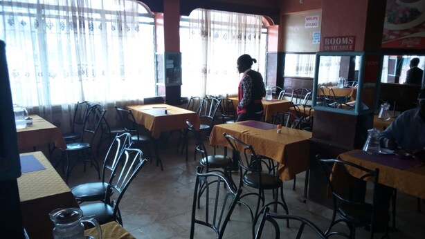 A restaurant with multiple tables and chairs, a person walking, and a sign indicating Wi-Fi availability. - Kwiremia Hotel (Embu)
